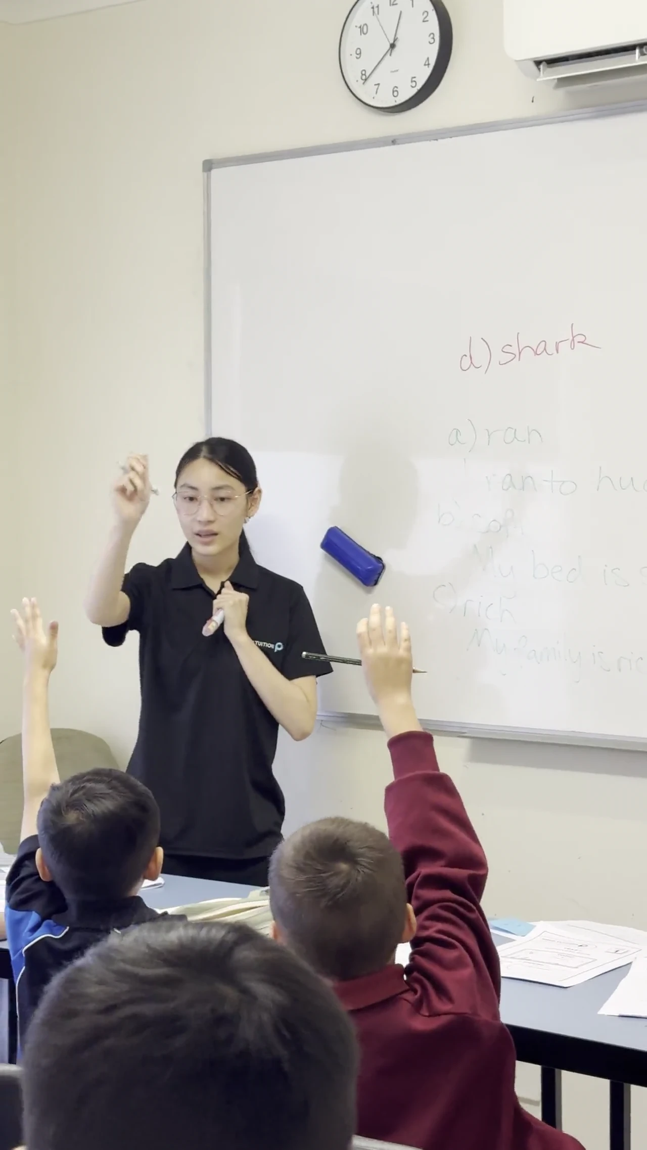 A Signal Education tutor teaching an English lesson at the whiteboard while students put their hands up